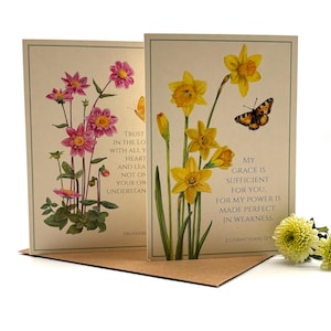 May include: Two rectangular greeting cards featuring botanical illustrations. The left card shows pink flowers and text from Proverbs. The right card displays yellow daffodils, a butterfly, and the text My grace is sufficient for you.