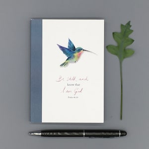 Może przedstawiać: Biała kartka z ilustracją niebieskiego i zielonego kolibra. Na kartce widnieje tekst "Be still, and know that I am God. Psalm 46:10" napisany kursywą.