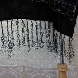May include: A black shawl with long, delicate fringe. The fabric appears to be a dark, possibly velvet material, with intricate detailing along the edge. The fringe hangs down, creating a textured effect.