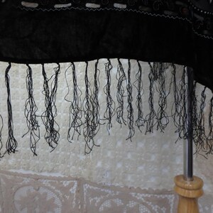 May include: Black fabric with a fringed edge. The fabric appears to be a dark, possibly velvet material. The fringe is made of thin, black threads. The fabric is decorated with white and silver embellishments.