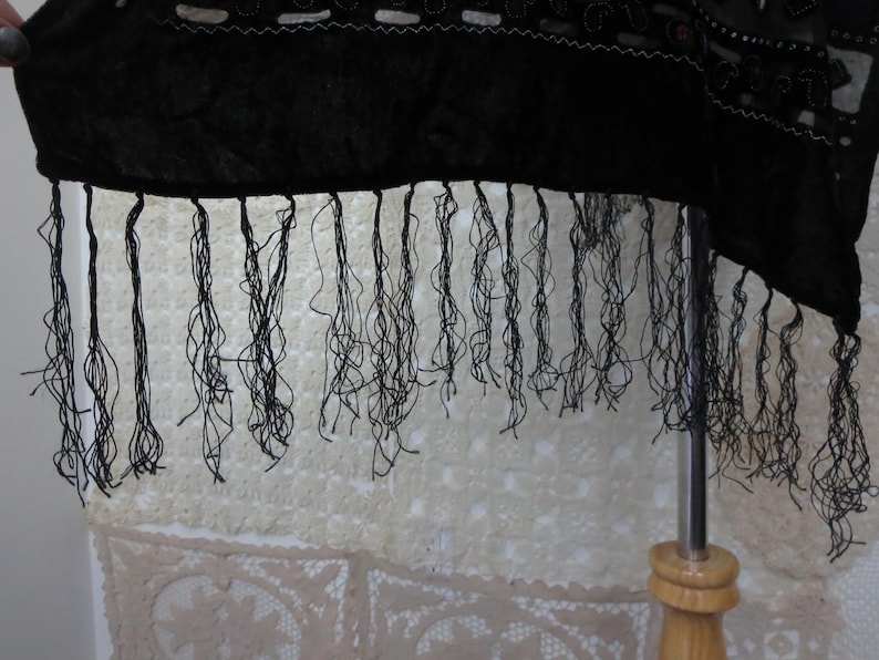May include: Black fabric with a fringed edge. The fabric appears to be a dark, possibly velvet material. The fringe is made of thin, black threads. The fabric is decorated with white and silver embellishments.