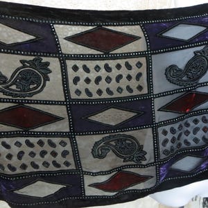 May include: A black, sheer scarf with a patchwork design. The scarf features squares in gray, purple, and burgundy, adorned with paisley and diamond patterns. The edges are trimmed with small, silver beads.