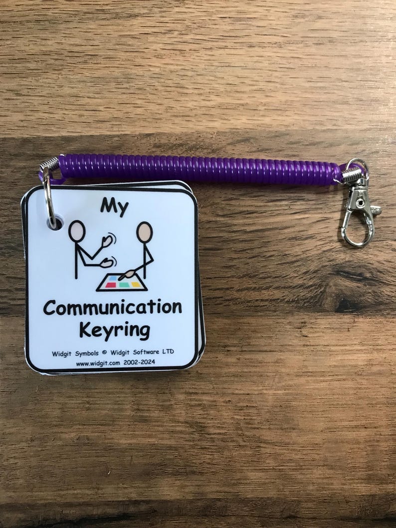 Puede incluir: Una tarjeta blanca con texto negro y una ilustraci&oacute;n simple de figura de palo. La tarjeta dice "My Communication Keyring" e incluye el nombre de la empresa y el sitio web. La tarjeta est&aacute; unida a un llavero de espiral morado.