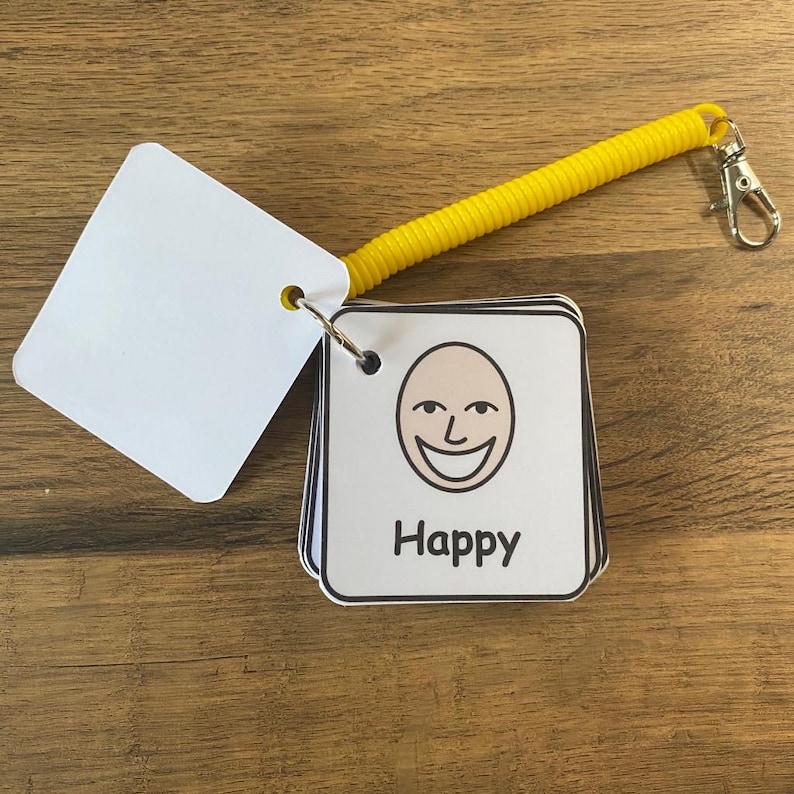 Puede incluir: Un conjunto de tarjetas blancas con bordes negros y un llavero de espiral amarillo. Cada tarjeta presenta una expresi&oacute;n facial diferente y la palabra "Happy" impresa debajo de la expresi&oacute;n.