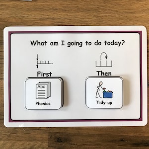 May include: A visual schedule for children with two steps: "First" and "Then". The first step is "Phonics" and is represented by a stack of papers with the letters "Abc" on top. The second step is "Tidy up" and is represented by a stick figure putting toys in a blue bin.