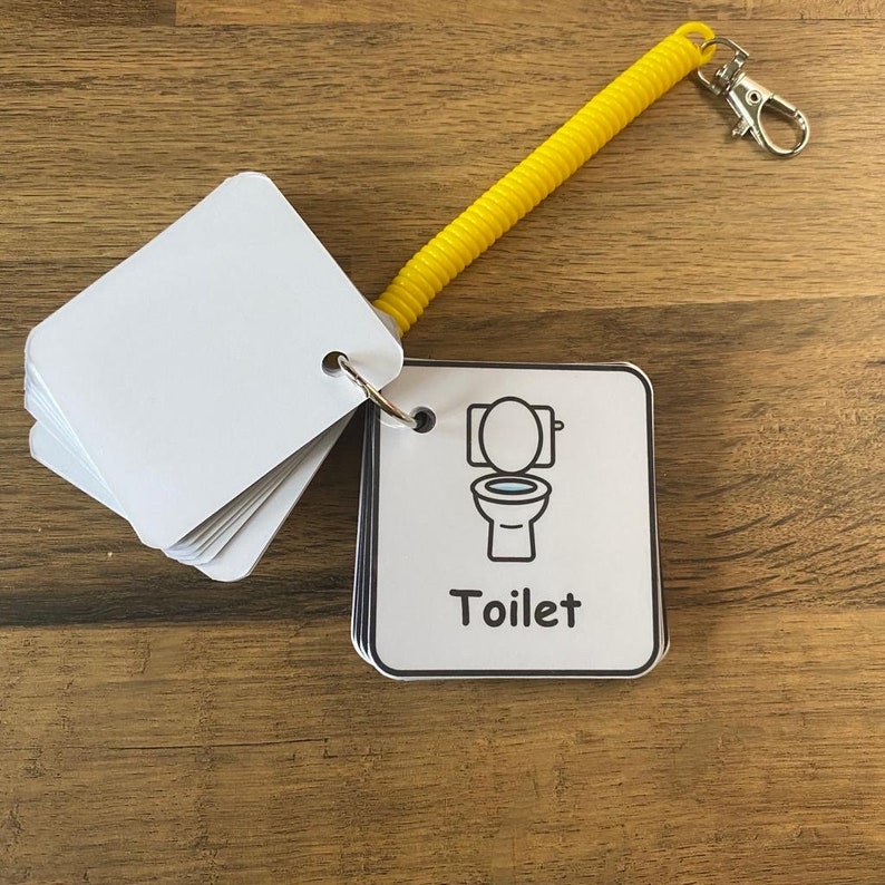 Puede incluir: Un conjunto de tarjetas de memoria blancas con una ilustraci&oacute;n en blanco y negro de un inodoro y la palabra "Toilet" en una tarjeta blanca. Las tarjetas est&aacute;n unidas a un llavero de espiral amarillo.