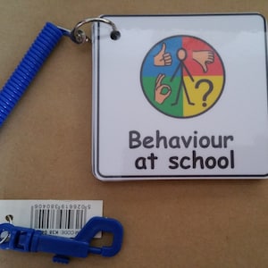 May include: A white card with a blue, green, yellow, and red circle with a stick figure in the middle. The circle has different hand gestures in each quadrant. The card says "Behaviour at school". The card is attached to a blue retractable keychain.