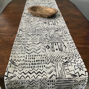May include: A black and white geometric patterned table runner with a wooden bowl on top. The runner is on a dark wood table.