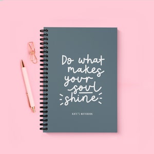 Könnte beinhalten: Ein graues Spiralnotizbuch mit dem Text "Do what makes your soul shine" in weißer Schrift. Das Notizbuch trägt den Text "KATE'S NOTEBOOK" unten.