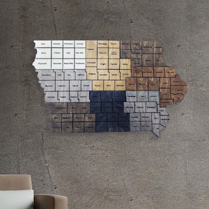 May include: A wooden map of the state of Iowa, with each county represented by a different colored square. The map is mounted on a gray wall, with a brown armchair in the foreground.