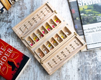 May include: A wooden pill organizer with seven compartments for each day of the week. The organizer is open and has colorful pills inside.