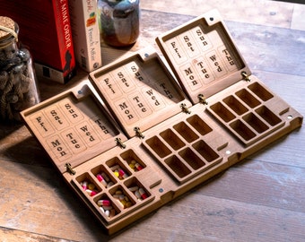 May include: A wooden pill organizer with seven compartments for each day of the week. The organizer has a hinged lid with days of the week labeled on each section. The lid is open and there are pills in the compartments.