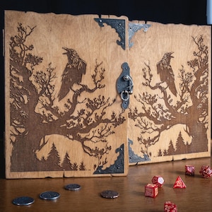 May include: A wooden box with a raven and tree design, featuring a metal clasp and corner accents. Several red dice and coins are scattered in front of the box, suggesting a tabletop game theme.