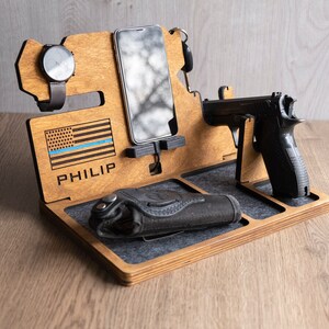 Puede incluir: Organizador de madera con una bandera estadounidense con una l&iacute;nea azul, el nombre "PHILIP" grabado, un soporte para reloj, un soporte para tel&eacute;fono, un soporte para pistola y una funda.