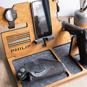 Puede incluir: Organizador de madera con compartimentos para un tel&eacute;fono, un reloj y una pistola. Presenta una bandera estadounidense con una l&iacute;nea azul y el nombre "PHILIP" grabado en ella.