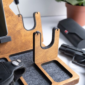 Puede incluir: Organizador de madera con m&uacute;ltiples compartimentos para guardar diversos art&iacute;culos. Cuenta con un soporte para tel&eacute;fono, un soporte para reloj, un soporte para pistola y una bandeja peque&ntilde;a. El organizador est&aacute; hecho de madera marr&oacute;n claro y tiene un forro de fieltro gris.
