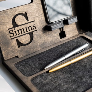 May include: A wooden valet tray with a personalised monogram of the letter "S" and the name "Simms". The tray has a grey felt lining and two slots for pens.