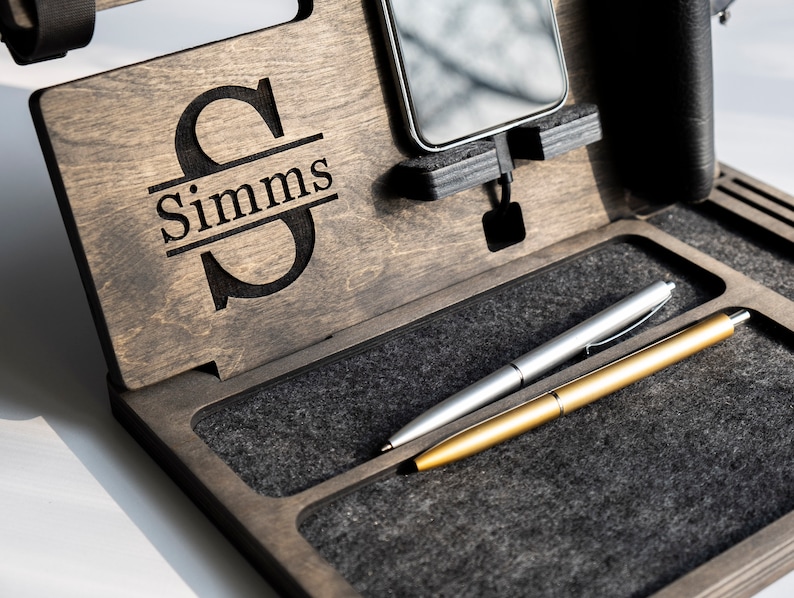 May include: A wooden valet tray with a personalised monogram of the letter "S" and the name "Simms". The tray has a grey felt lining and two slots for pens.