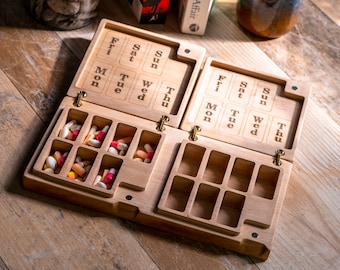 May include: A wooden pill box with seven compartments for each day of the week. The box is open and the compartments are filled with pills. The box is made of light wood and has a natural finish.