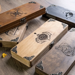 May include: Five wooden boxes with engraved designs. The boxes have metal hinges and decorative corners. The designs include a compass, a dragon, a sword and wings, a monogram, and a dice with the words "Roll Initiative".