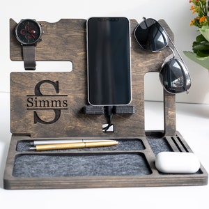 May include: A wooden organiser with a grey felt lining. It has slots for a phone, watch, sunglasses, and pens. The organiser is personalised with the name "Simms".