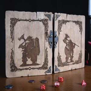 May include: Wooden game box with a hinged design, featuring engraved illustrations of a dwarf warrior with an axe and shield. The box is adorned with decorative borders and a metal clasp. Dice and coins are scattered on the wooden surface.