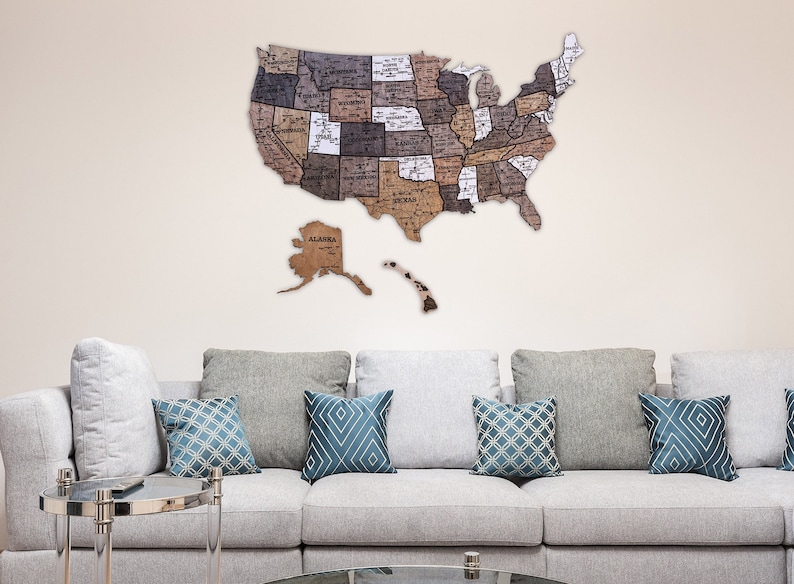 May include: A wooden map of the United States with each state outlined and labelled. The map is mounted on a wall above a grey sofa with blue patterned cushions.