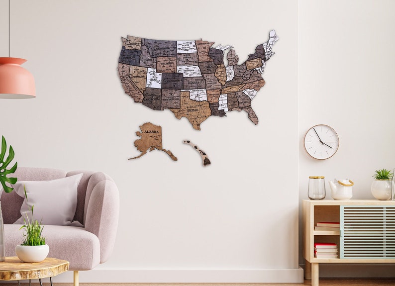 May include: A wooden map of the United States with each state outlined and labelled. The map is mounted on a white wall in a living room setting. The map is a light brown colour with darker brown accents.