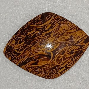 May include: A polished, brown and yellow gemstone with a unique pattern. The stone has a rounded, square shape and a glossy finish. The intricate design resembles a network of lines and swirls, creating a natural, organic aesthetic. This gemstone is ideal for jewelry making.