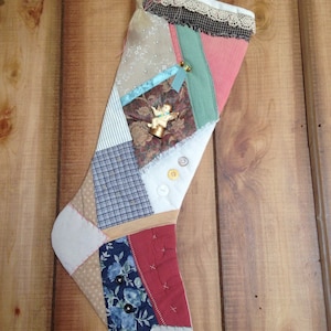 May include: A patchwork Christmas stocking with a variety of fabrics, including plaid, floral, and solid colors. The stocking is decorated with a small angel figurine and buttons.