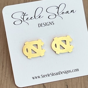 Op de afbeelding: Gouden oorbellen met het UNC Tar Heels logo. De oorbellen worden getoond op een witte kaart met de tekst "Steele Sloan Designs" en "www.SteeleSloanDesigns.com".