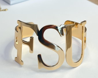 May include: Gold-toned metal bracelet with the letters FSU cut out. The bracelet is open and ready to be worn.