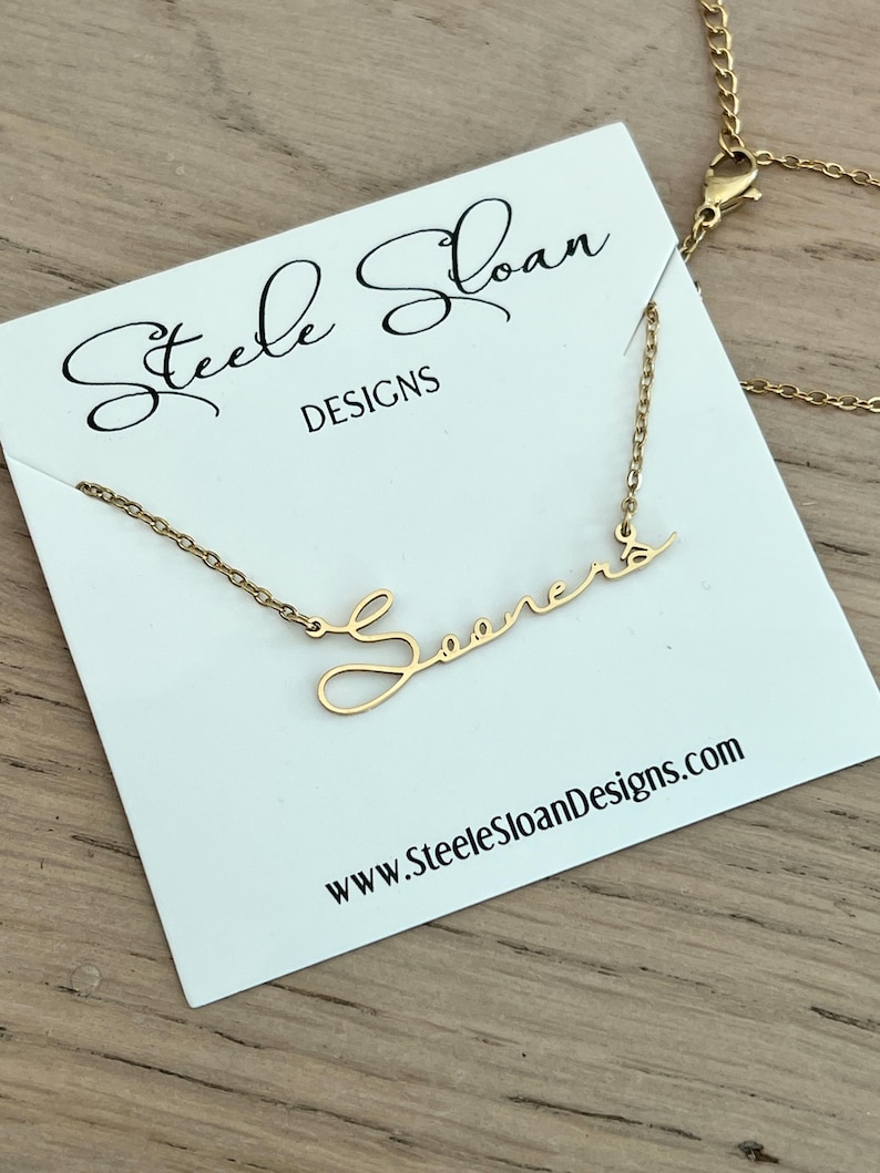 May include: Gold necklace with a cursive script pendant that says "Sooners". The necklace is on a white card with the text "Steele Sloan Designs" and "www.SteeleSloanDesigns.com".