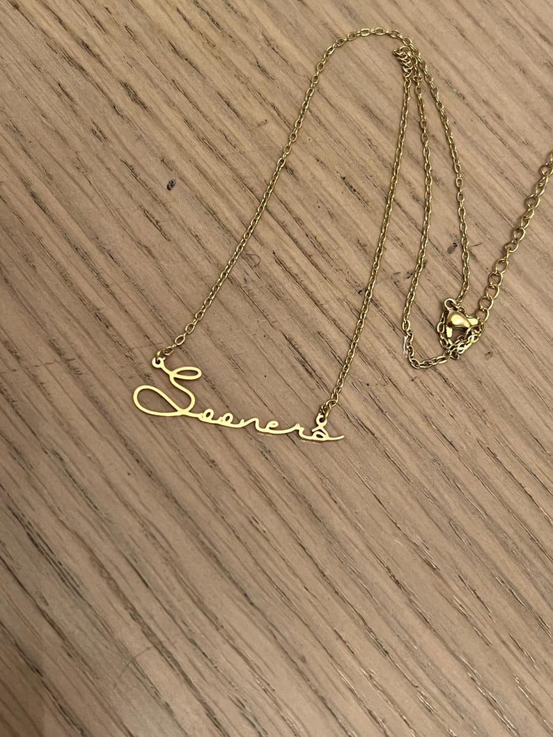 May include: A gold chain necklace with a cursive name pendant that says "Sooners".