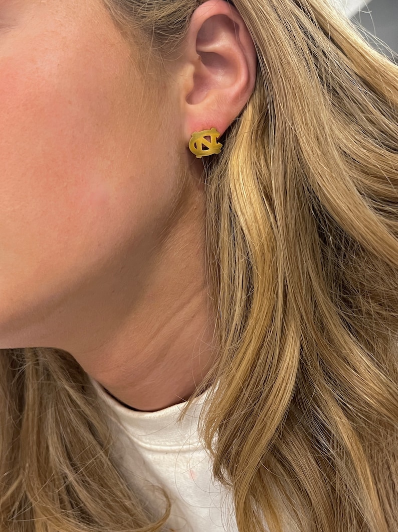 Op de afbeelding: Gouden oorbel studs met het logo van de University of North Carolina Tar Heels.