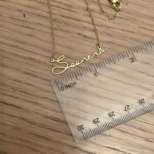 May include: Gold necklace with a cursive script pendant that reads "Sooners". The necklace is measured against a ruler, showing the pendant is about 1 inch long.