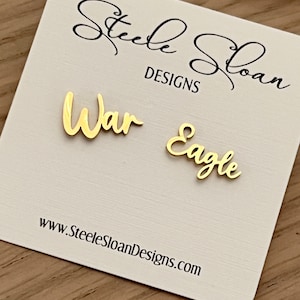 Pu&ograve; includere: Un biglietto bianco con le parole "Steele Sloan Designs" e "War Eagle" scritte in corsivo dorato. Il biglietto include anche l'indirizzo del sito web "www.SteeleSloanDesigns.com".