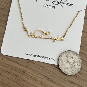 Op de afbeelding: Een goudkleurige ketting met de tekst "War Eagle" in script wordt getoond op een witte kaart. De kaart heeft bovenaan de tekst "Steele Sloan DESIGNS" en onderaan het websiteadres. Een munt ligt naast de kaart.