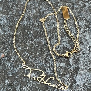 May include: Gold chain necklace with a cursive name pendant that says "Tara Vee" hanging from it.