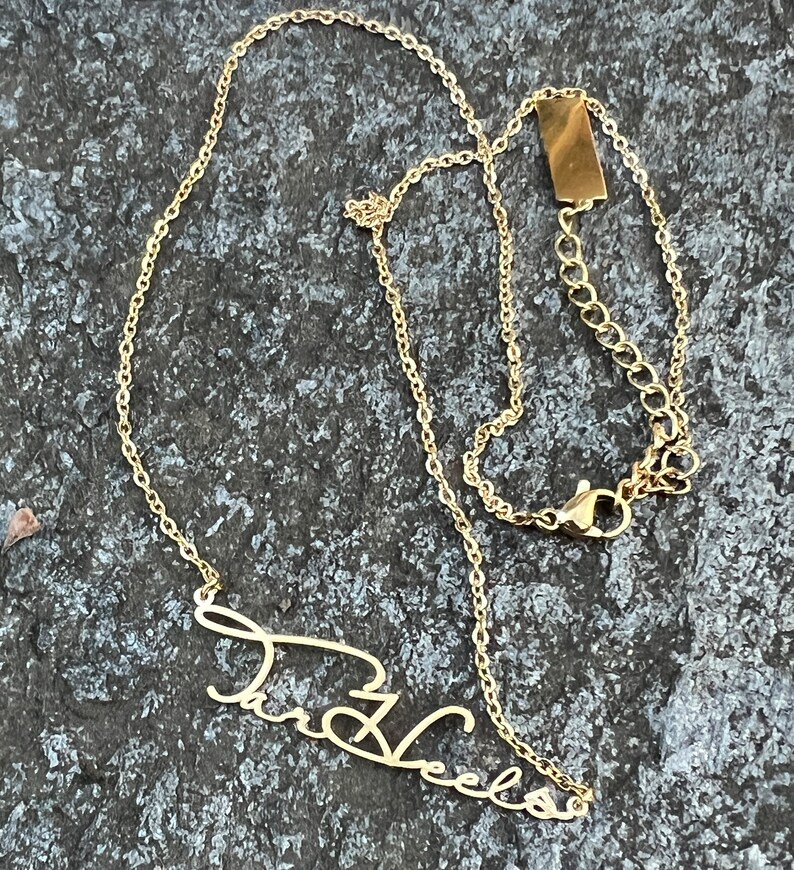 May include: Gold chain necklace with a cursive name pendant that says "Tara Vee" hanging from it.