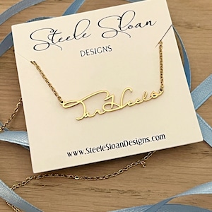 May include: A gold necklace with the name "Tar Heels" written in cursive script on a white card with the text "Steele Sloan Designs" and the website address "www.SteeleSloanDesigns.com".