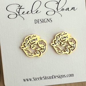 Może przedstawiać: Para złotych kolczyk&oacute;w z logo UNC. Kolczyki są prezentowane na białej kartce z tekstem "Steele Sloan Designs" i "www.SteeleSloanDesigns.com".