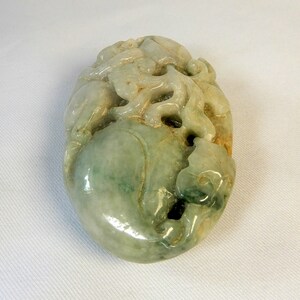 May include: A green jade carving of a mythical creature with intricate details. The carving is oval shaped and has a smooth, polished finish.