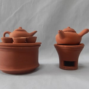 May include: Two terracotta teapots with matching bases. The teapot on the left has three small cups on a round base. The teapot on the right has a single base with a small opening.