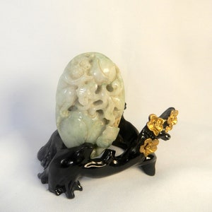 May include: A carved jade pendant depicting a mythical creature, possibly a dragon, with intricate details. The pendant is displayed on a black wooden stand with gold accents.