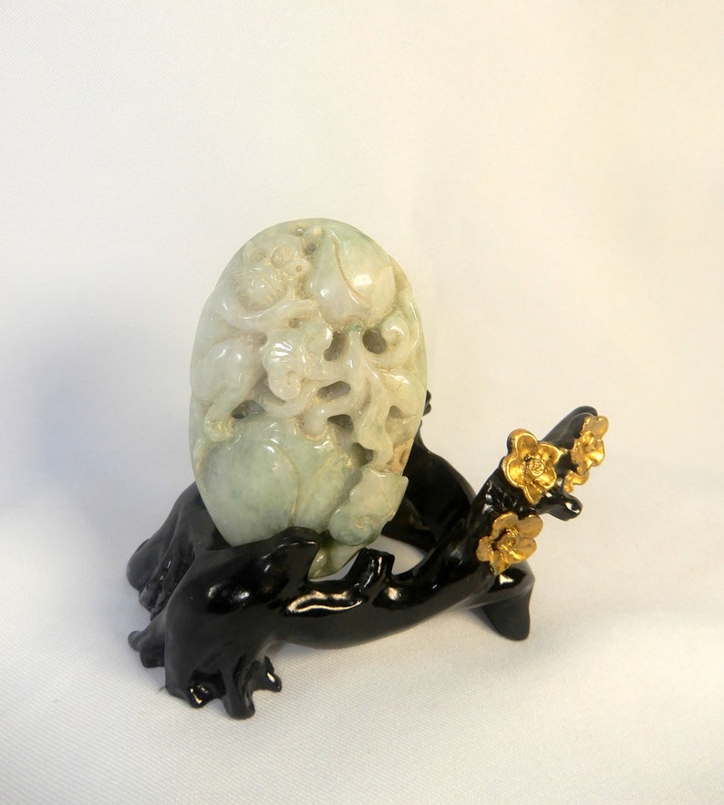 May include: A carved jade pendant depicting a mythical creature, possibly a dragon, with intricate details. The pendant is displayed on a black wooden stand with gold accents.