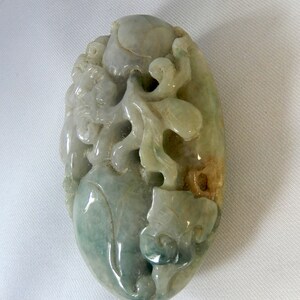 May include: A green jade pendant carved with intricate floral designs. The pendant is oval shaped and has a smooth, polished surface.