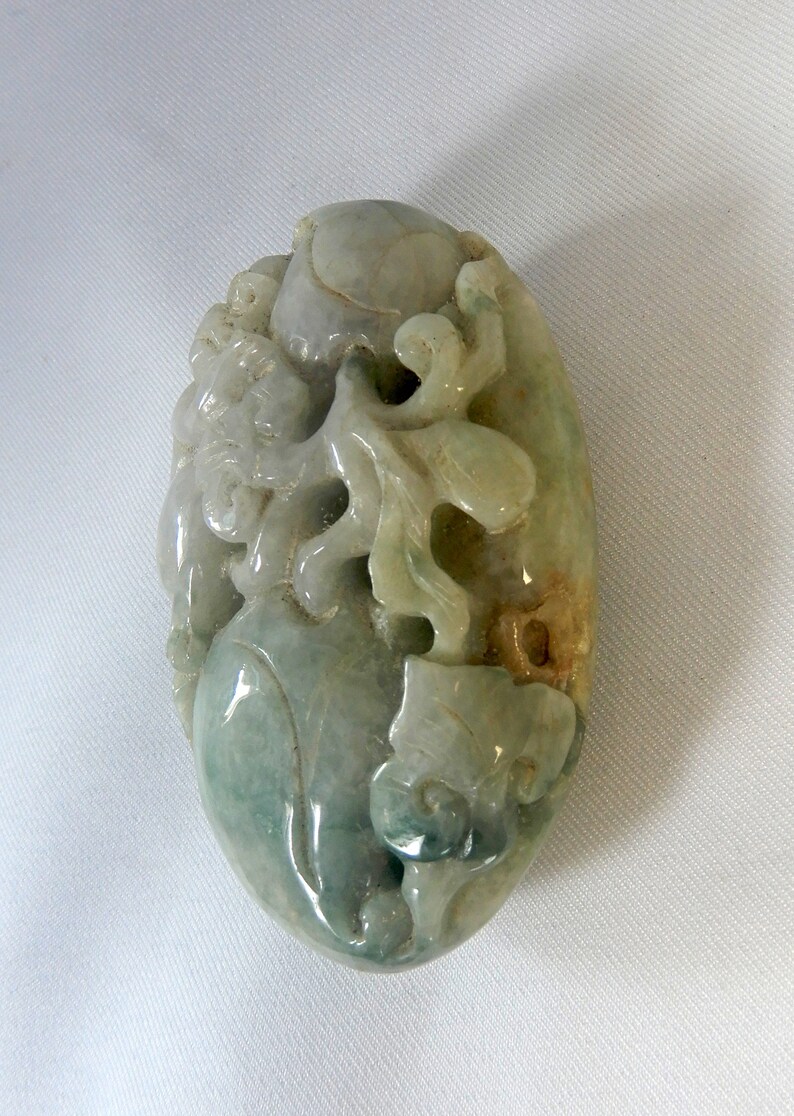 May include: A green jade pendant carved with intricate floral designs. The pendant is oval shaped and has a smooth, polished surface.