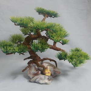 Op de afbeelding: Een miniatuur bonsai boom met groene bladeren en een bruine stam. De boom staat op een rotsbasis met een klein beeldje. Deze decoratieve bonsai is ideaal om een vleugje natuur aan elke ruimte toe te voegen.