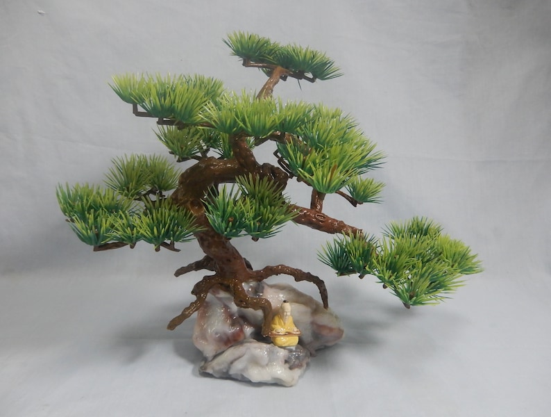Op de afbeelding: Een miniatuur bonsai boom met groene bladeren en een bruine stam. De boom staat op een rotsbasis met een klein beeldje. Deze decoratieve bonsai is ideaal om een vleugje natuur aan elke ruimte toe te voegen.
